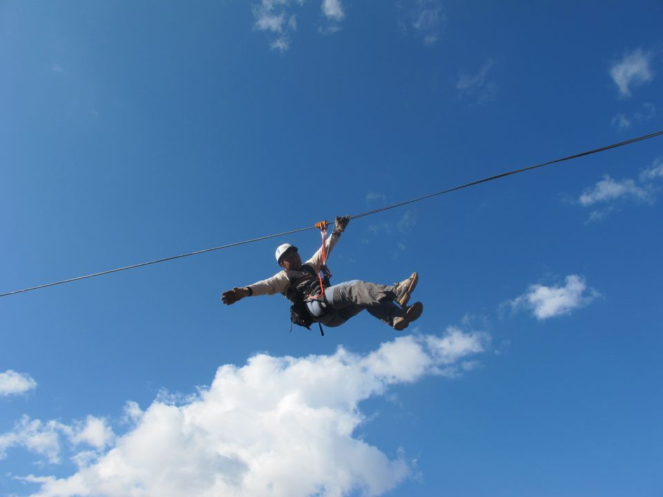 Person wearing a helmet riding a zipline cable under a blue sky