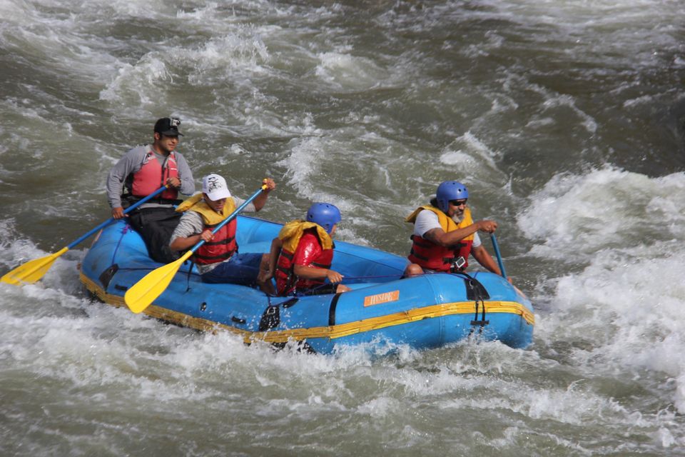 Rafting boat with four paddlers and a guide in white water
