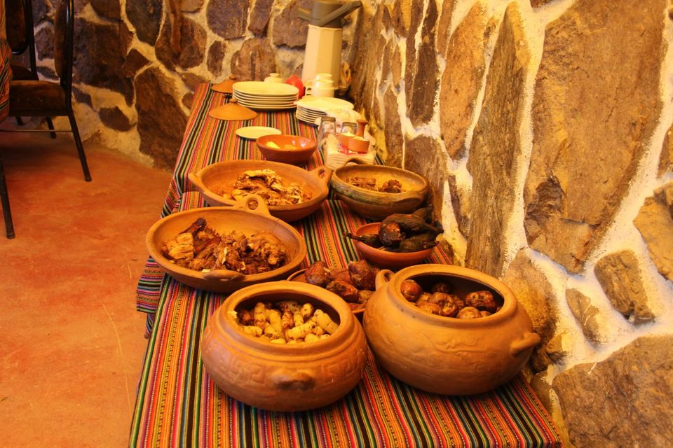 Table with pachamanca, potatoes and sweet potatoes served in clay pots