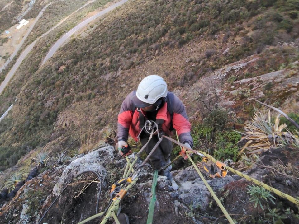 Guía de escalada con casco asegurado con cuerdas sobre la pared, con el valle al fondo