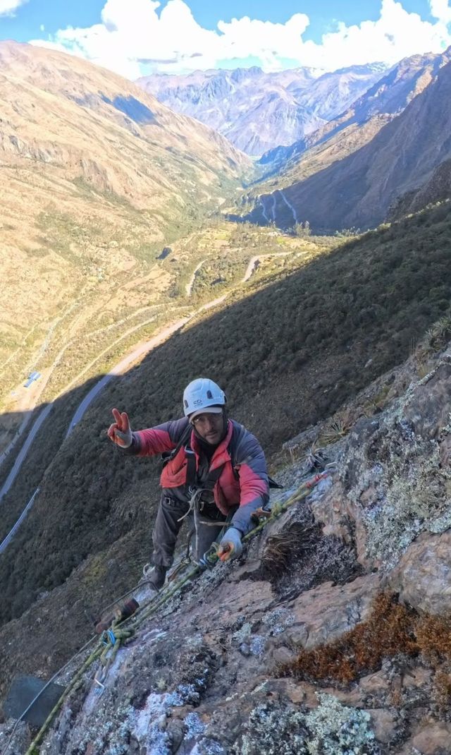 Guía de Sota Adventure en la pared de roca saludando, con el valle y la carretera abajo